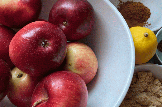 a bowl of apples, a lemon, and several bowls of baking ingredients