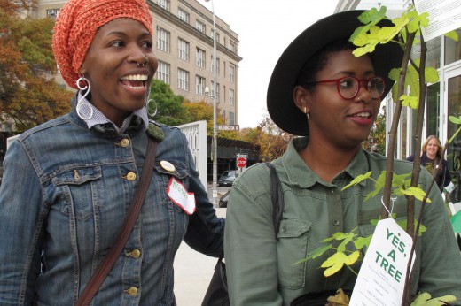 two smiling women, one holding a potted tree